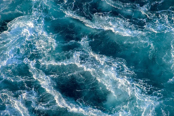 Fırtınalı okyanus dalgaları batan güneşin ışığıyla aydınlanıyor. Şeffaf. Lacivert. Mavi. Geçmişi. Desen.