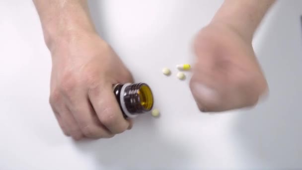 Pastillas médicas, vitaminas priparaty en la mano sobre un fondo blanco, dispersar recoger, quitar el frasco, se acumula en la mesa — Vídeo de stock