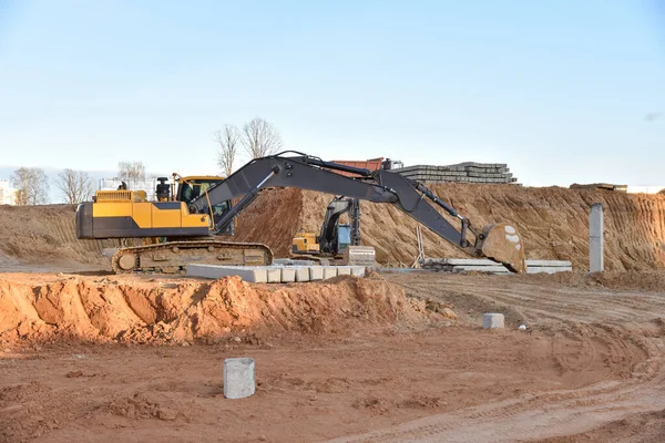Excavator during excavation at construction site. Backhoe on foundation work in sand pit. Groundworks, site levelling, construction of reinforced ground beams on piled foundations .