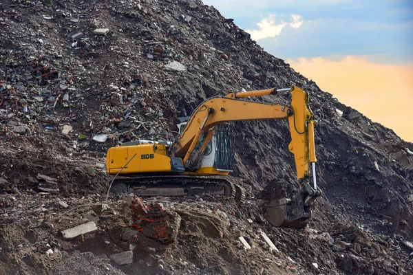Excavator at landfill for the disposal of construction waste. Backhoe digs gravel and concrete crushing. Recycling old concrete and asphalt from demolition. Salvaging and removal building materials