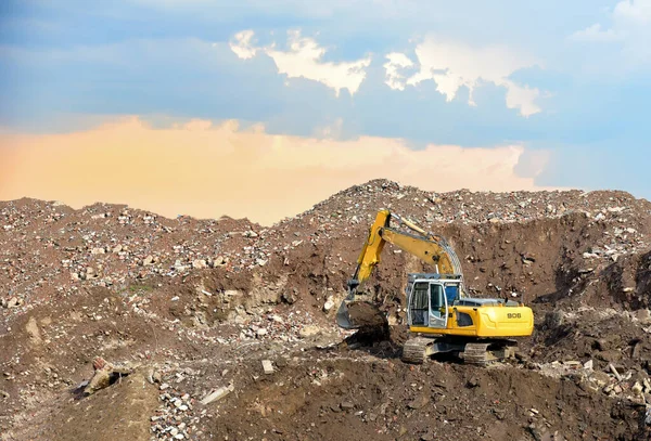 Excavator at landfill for the disposal of construction waste. Backhoe digs gravel and concrete crushing. Recycling old concrete and asphalt from demolition. Salvaging and removal building materials