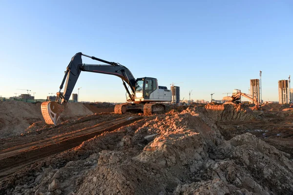 Excavators during earthworks at construction site. Backhoe the digging pit for construct building foundation. Paving out sewer line. Construction machinery for excavating, loading, lifting and hauling