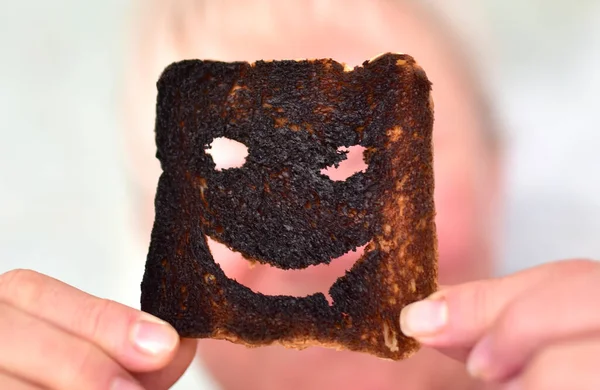 Burnt toast bread slices. Woman holds in hands a burnt slice of toast with an angry face expressing the emotion of sadness or sarcasm. Unsuccessful ooking breakfast before a work day or weekend.