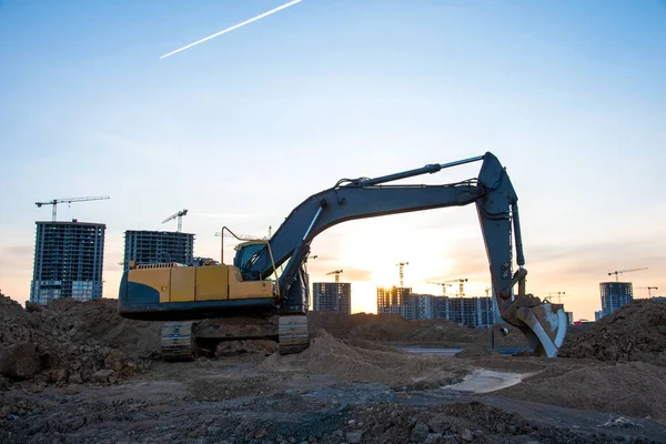 Excavator during earthmoving at construction site on sunset background. onstruction machinery for excavating. Tower cranes lifting a concrete bucket for pouring of concrete into formwork.