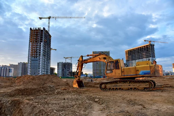 Excavator during earthmoving at construction site on sunset background. Backhoe digs ground for underground sewage and water pipes. onstruction machinery for excavating.