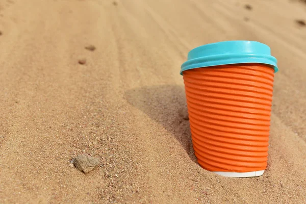 Discarded Paper coffee cup on sand at beach. Disposable coffee cup on sandy background. The problem of environmental pollution. Pile of abandoned garbage, including food waste, fast food packaging