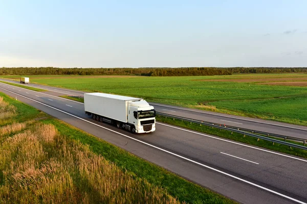 Truck with semi-trailer driving along highway on the blye sky background. Goods delivery by roads. Services and Transport logistics. Soft focus.