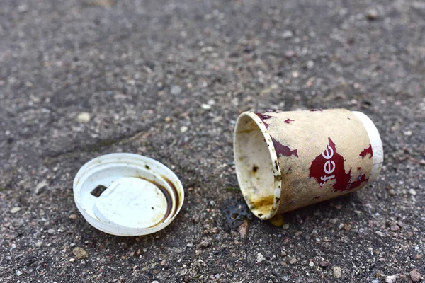 Crumpled a paper coffee cup on asphalt. Discarded disposable coffee cup with a plastic lid on road. Out of shape crushed paper cup. Abandoned garbage of disposable cups.