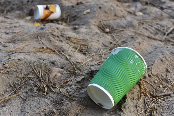 Discarded Paper coffee cup on ground. Disposable coffee cup on sand. The problem of environmental pollution. Pile of abandoned garbage, including food waste, fast food packaging