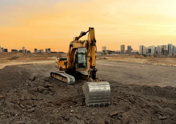 Excavator on earthworks at construction site on sunset background. Digging a foundation pit and a trench for laying sewer pipes.  Renovation and construction of a residential multi-storey building.