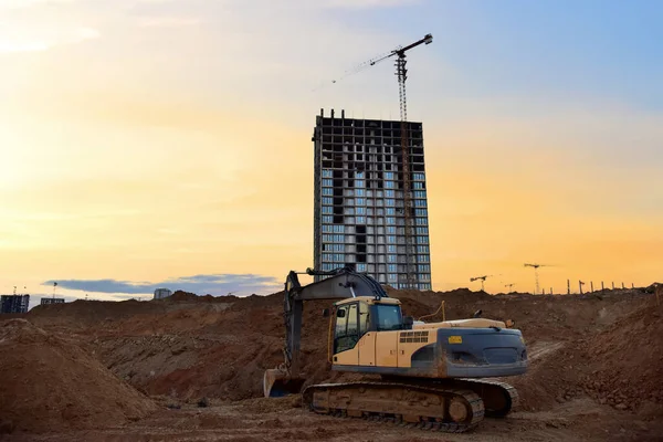 Excavator on earthworks at construction site on sunset background. Digging a foundation pit and a trench for laying sewer pipes.  Renovation and construction of a residential multi-storey building