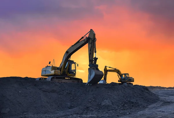 Excavator working on earthmoving at open pit mining on amazing sunset background. Backhoe digs sand and gravel in quarry. Heavy construction equipment during excavation at construction site