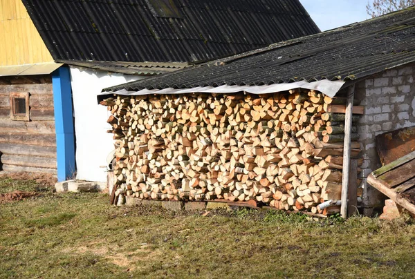 Chopped logs of firewood piled under the roof in the village  in a backyard. Fuel for stove heating. Wooden firewood stacked. Pile of chopped dry logs. Out of focus