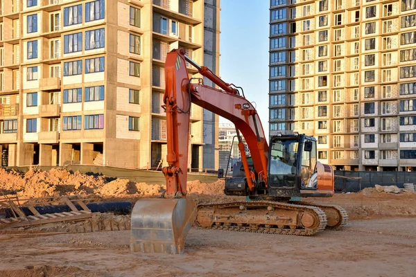 Excavator working at construction site on earthworks. Backhoe digging building foundation. Paving out sewer line. Construction machinery for excavating, loading, lifting and hauling of cargo