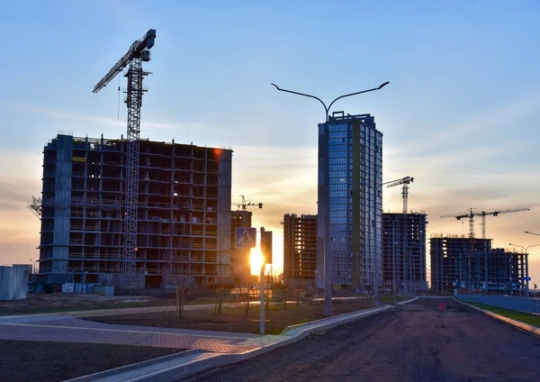View on the large construction site with tower cranes and buildings on sunset background. Multi-storey residential building is being constructed use of crane. Concept of renovation program