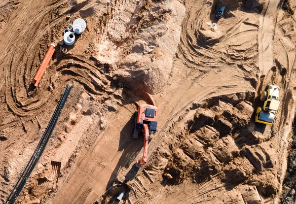 Installation of storm sewers and construction of a road in a new residential area. Excavator on earthworks, view from the top, view from the drone. Roadworks soil compactor