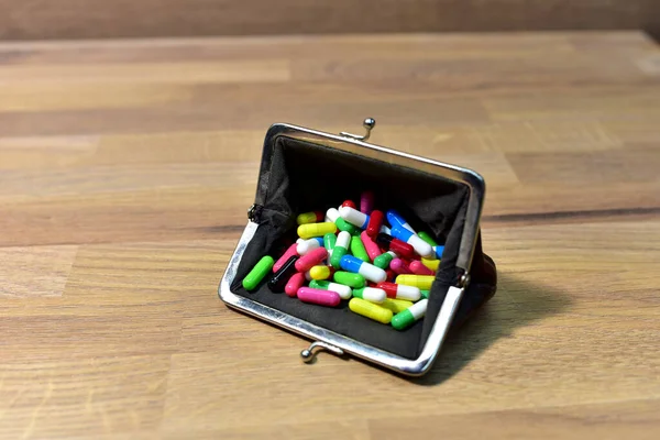 Pills in wallet on wooden background. Multicolored pharmaceutical pills, medical tablets and capsules in purse. Pill addiction concept. Spending money for drugs at the pharmacy. Maintaining health