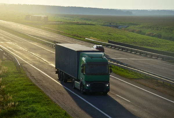 Semi truck transporting sea container on highway on sunset background. Shipping Containers Delivery, Maritime Services and Transport logistics