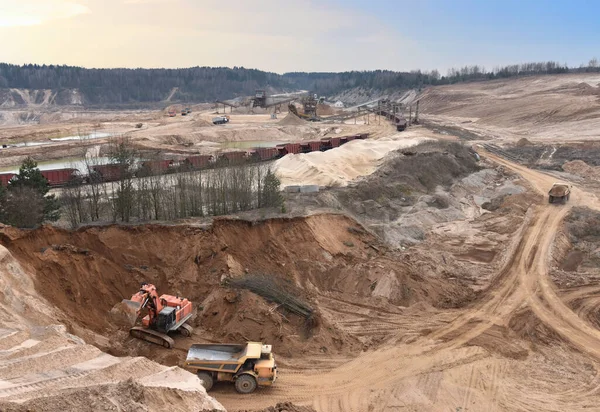 Excavator load sand in heavy mining truck at open-pit. Heavy machinery working in mining quarry. Plant for production sand and gravel for construction industry. Conveyor belt for crushing stone.