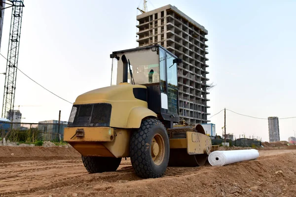 Vibro Roller Soil Compactor leveling soil at construction site. Excavator and vibration single-cylinder road roller during the construction of road. Road work project. Laying new asphalt