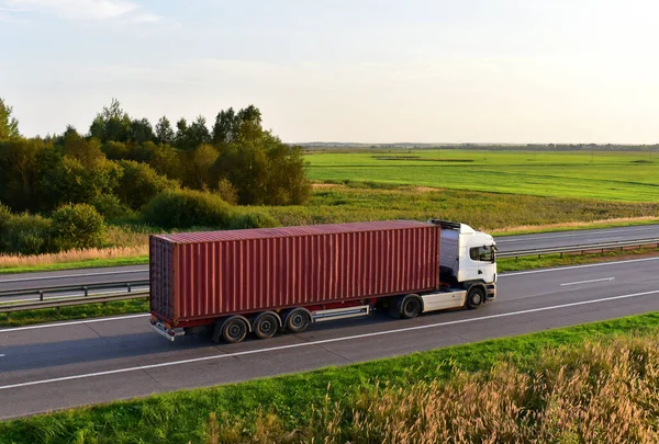 Semi truck transporting sea container on highway on sunset background. Shipping Containers Delivery, Maritime Services and Transport logistics.