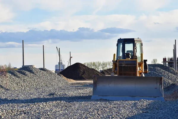 Bulldozer moves gravel during on road work at construction site. Dozer leveling stones for laying asphalt on a new freeway. Heavy machinery for earth-moving. Roadwork and road construction concept