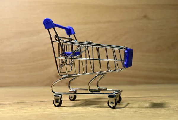 Shopping cart on wooden background. Mini shopping trolley or shopping basket cart.