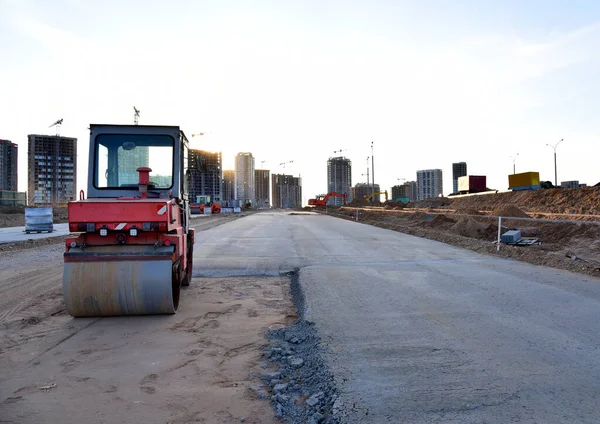 Paving roller machine during road work at construction site for paving works. Asphalt paver Road roller for Screeding the sand and road concreting. Tower cranes in action under buildings