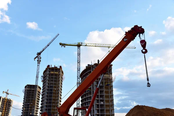 Boom of a truck crane with a hook at a construction site against the background of residential buildings and tower cranes under construction. Erection multi-storey residential building