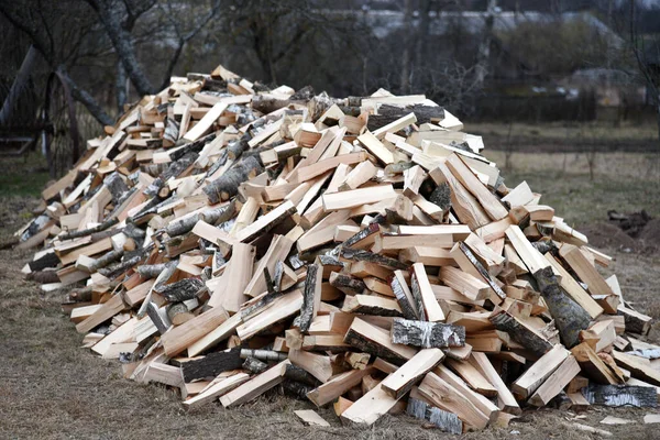 Large pile of chopped birch firewood on ground in the village. Fuel for stove heating. Wooden firewood stacked. Pile of chopped dry logs. Out of focus