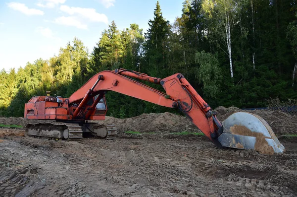 Excavator during groundwork at forest area for construction new road. Orange backhoe on road work, land clearing, grading, excavation, utility trenching. Earth-moving equipment. Open pit development