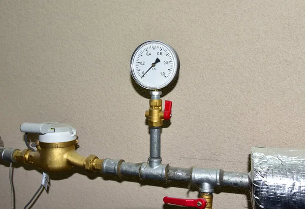 Heating system in boiler room at home. Round mechanical pressure gauge for measuring pressure and temperature control. Gauges near the heating pipes with insulation coating. Oil and gas pipeline