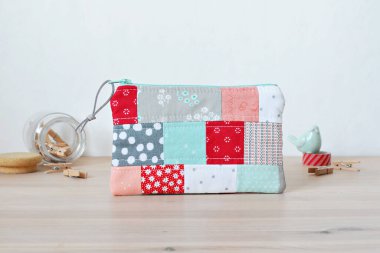 Renkli yamalı, yorgan kaplı fermuar kesesi, iğneli kavanoz, nane kuşu ve beyaz masanın üzerindeki kırmızı washi bandı.