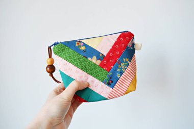 El ele tutuşan renkli yamalı kavramsal çanta fermuar ve beyaz üzerinde ahşap boncuklar