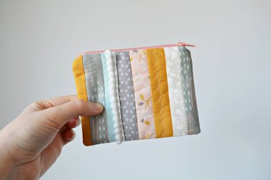 El ele tutuşan yamanmış fermuar kesesi ve beyaz üzerine altın saç tokaları.