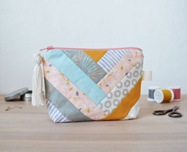 Patchwork fermuar kesesi, püsküllü fermuar havuzu, iplik makaraları, küçük makas ve çiviler ahşap masanın üzerindeki metal kavanozda.
