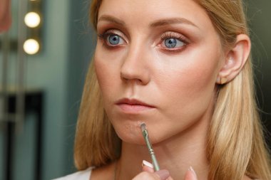 Makyaj yapma süreci. Makyaj sanatçısı modelin yüzünde bir fırça ile çalışıyor. Bir güzellik salonunun iç genç bir kadının portresi. Cilde ton uygulama.