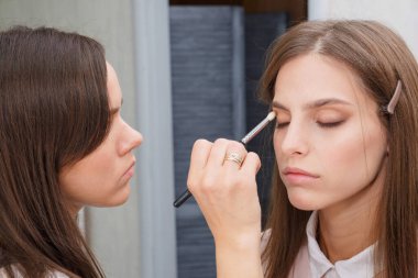 Makyaj yapma süreci. Makyaj sanatçısı modelin yüzünde bir fırça ile çalışıyor. Bir güzellik salonunun iç genç bir kadının portresi. Cilde ton uygulama.