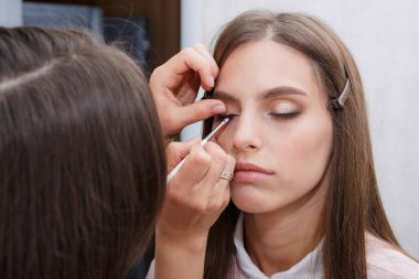 Makyaj yapma süreci. Makyaj sanatçısı modelin yüzünde bir fırça ile çalışıyor. Bir güzellik salonunun iç genç bir kadının portresi. Cilde ton uygulama.