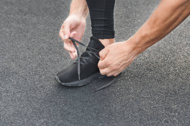 Genç erkek koşucu sporcu antrenmanı yapıyor ve şehir dışında spor yapıyor. Koşu ayakkabısı bağlayan adam.