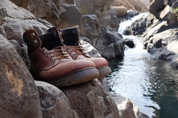 Viejas botas de senderismo frente a la cascada —  Fotos de Stock