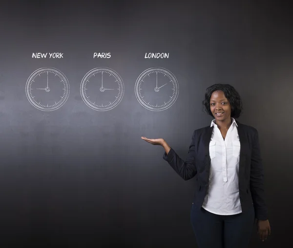 South African or African American woman teacher or student with New York Paris and London chalk time zone clocks on blackboard