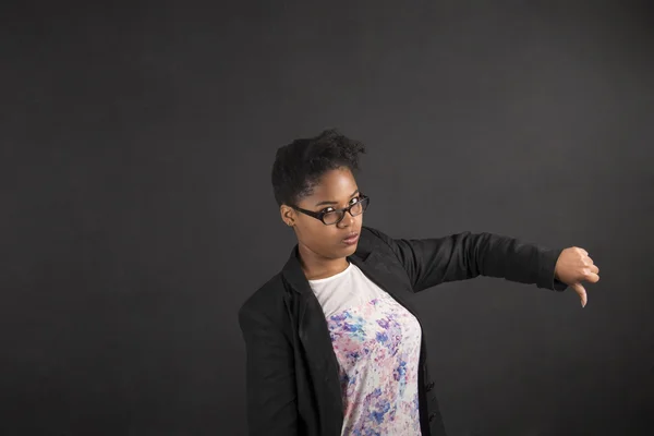 African woman with thumbs down hand signal on blackboard background — Stock fotografie