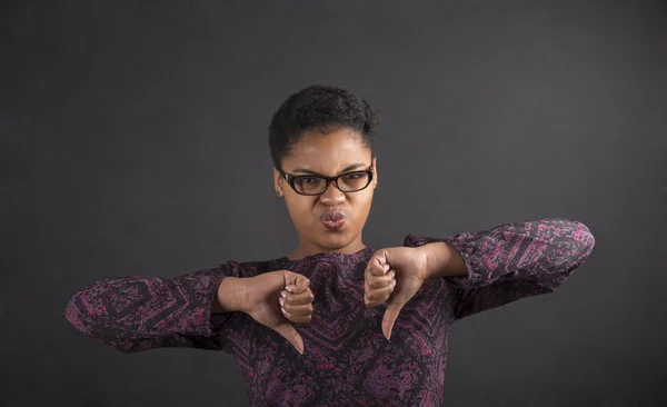 African woman with thumbs down hand signal on blackboard background — Stock fotografie