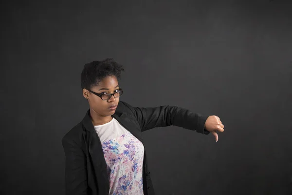 African woman with thumbs down hand signal on blackboard background — Stock fotografie