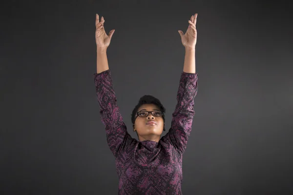 South African or African American woman teacher or student reaching for the sky on blackboard background — Zdjęcie stockowe