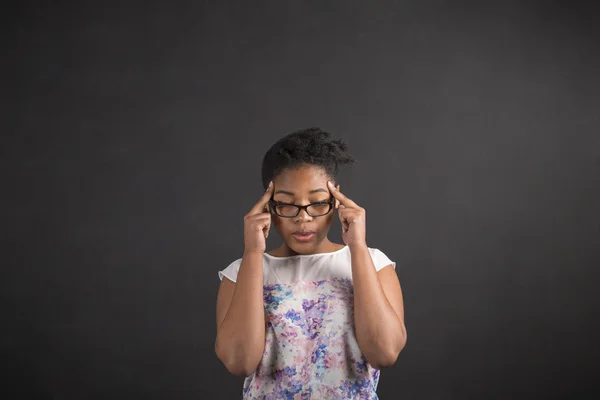 African woman with fingers on temples thinking on blackboard background — 图库照片