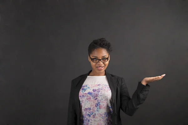 African woman holding hand out on blackboard background — Stock fotografie