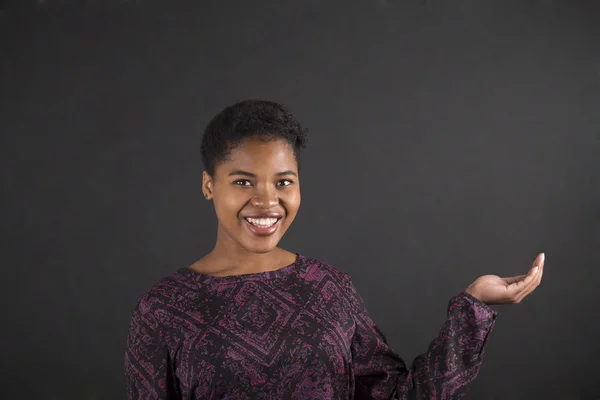 African woman holding hand out on blackboard background — Stockfoto