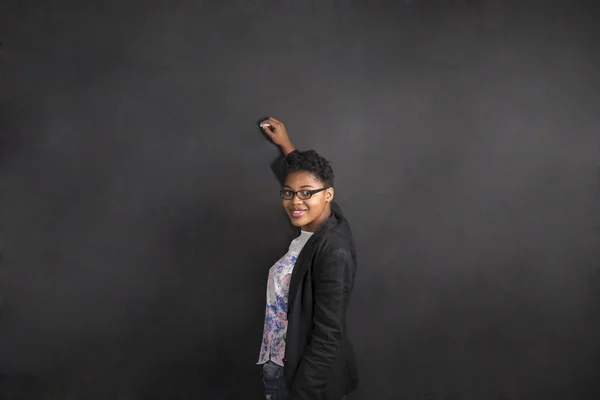 South African or African American woman teacher writing on chalk black board background — Stock Photo, Image